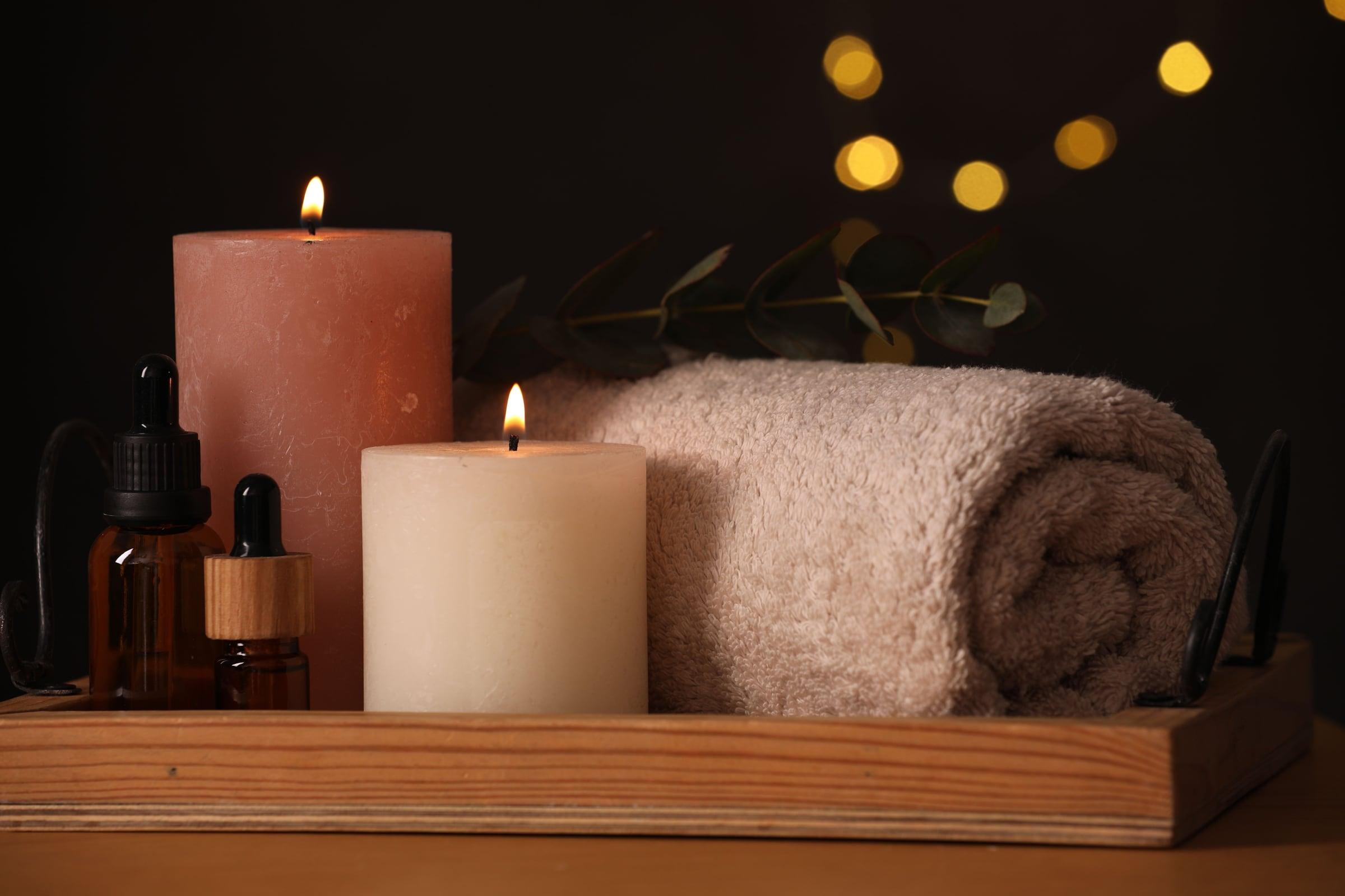 Gjöf úr húsinu — kerti, nuddolíur og upprúlluð handklæði á viðarbakka í hlýrri birtu